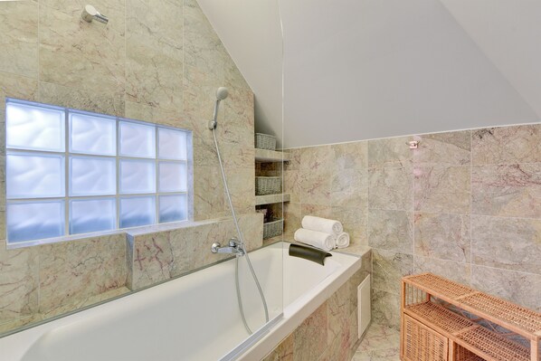 A modern bathroom with a glass-enclosed bathtub, a showerhead, and a window with frosted glass panels.