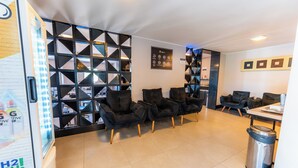 Un moderno vestíbulo de hotel con sofás de cuero negro, piso de baldosas y un panel divisor de pared geométrico negro.