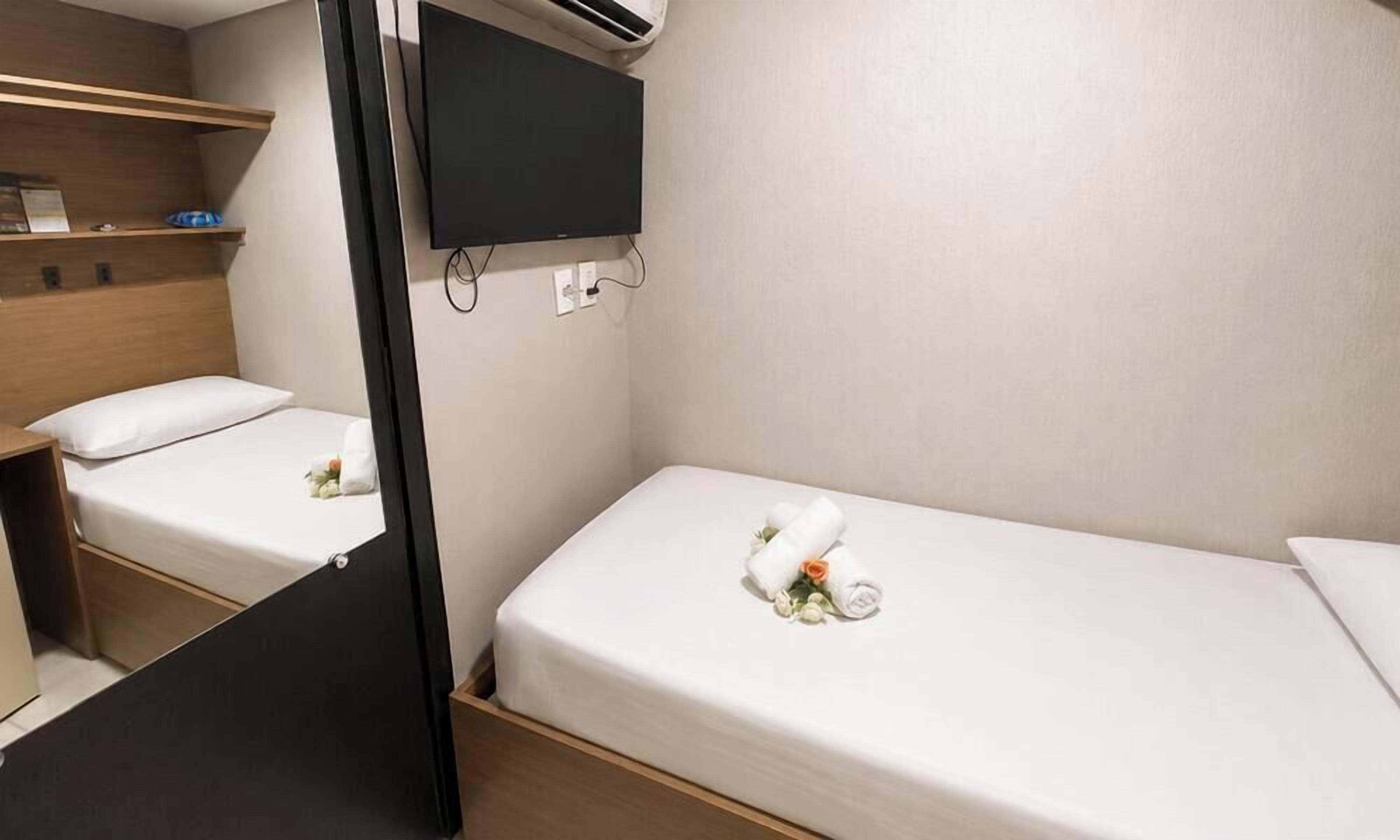 A compact room with two single beds, a mounted TV, and a wooden shelf.