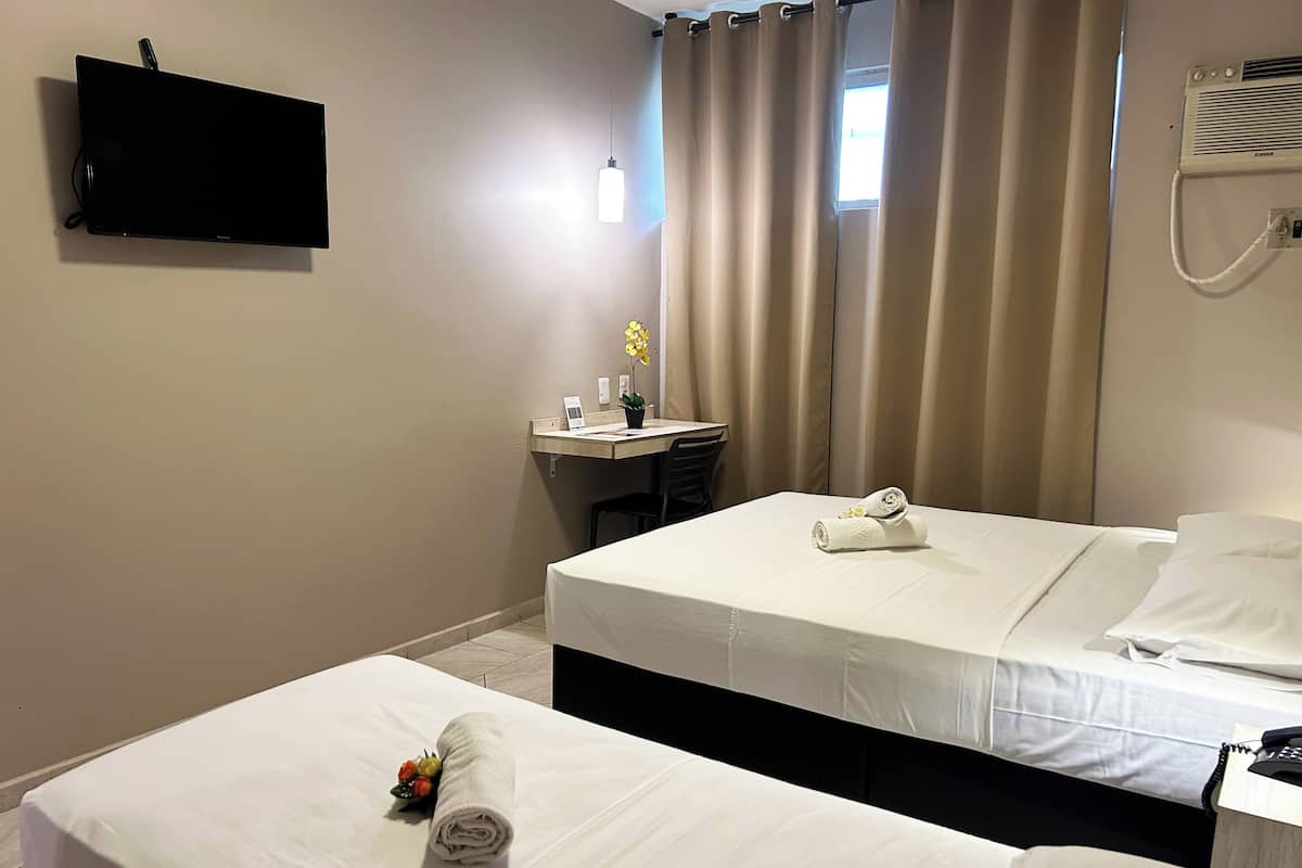 Ett hotellrum med två sängar, ett skrivbord, en stol, en platt-TV och ett fönster med gardiner.