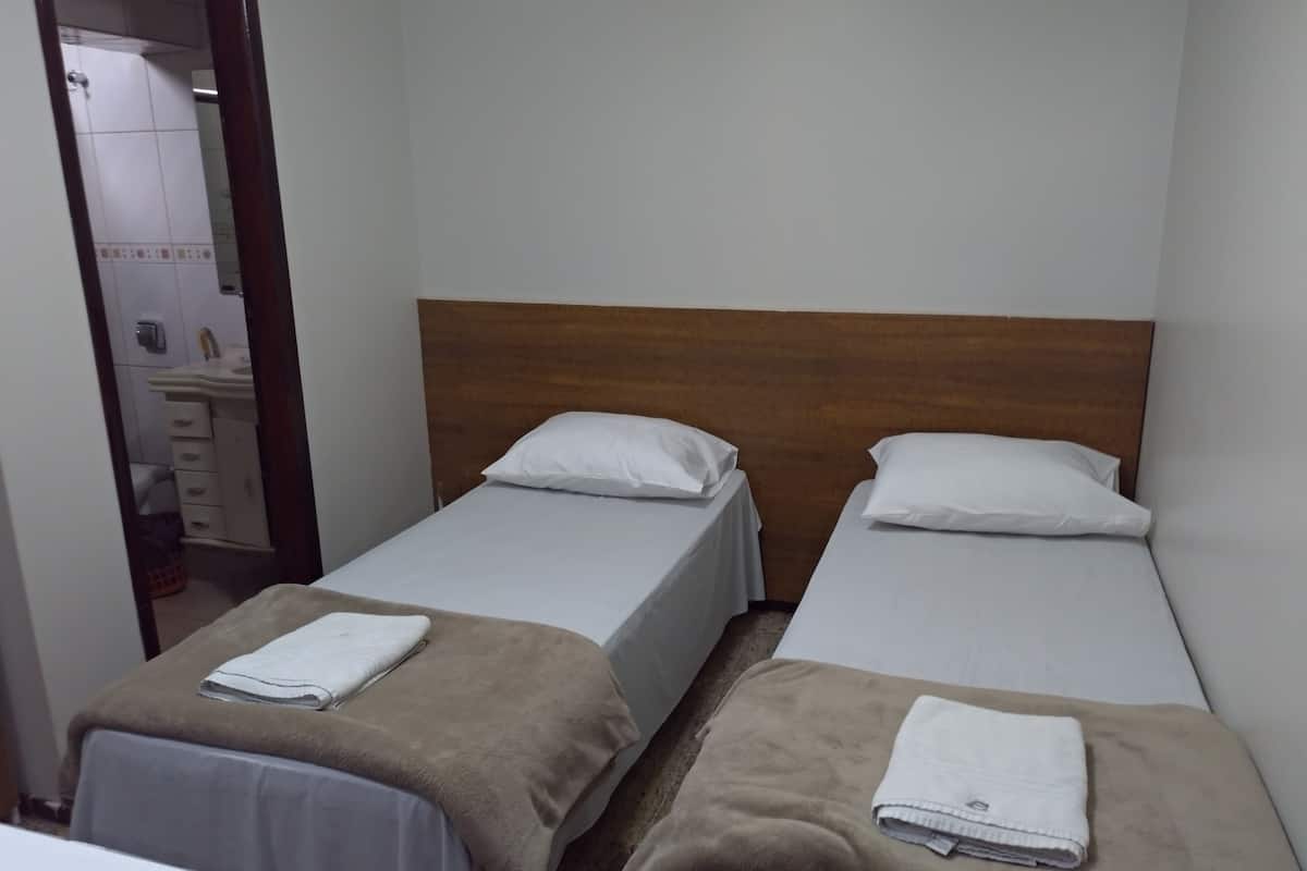 Ett hotellrum med två separata sängar, en sänggavel i trä, ett badrum som syns genom en öppen dörr och ett litet bord med en stol.