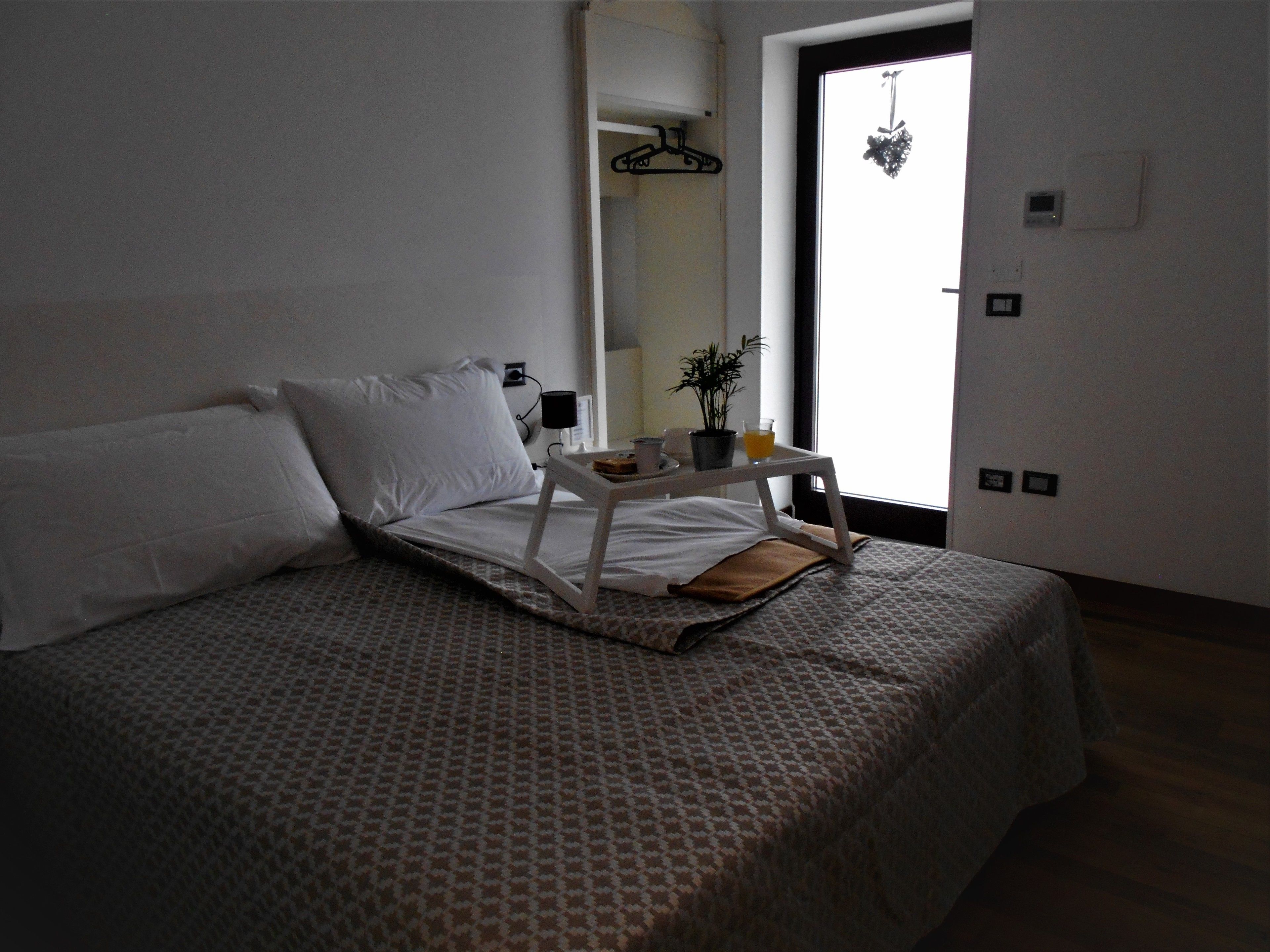 A neatly made bed with a patterned bedspread, a bedside table with a lamp, a small potted plant, and a cup of coffee.