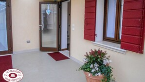 A building entrance with a glass door, red shutters, and a potted plant. - Locanda Righetto (Quinto di Treviso)