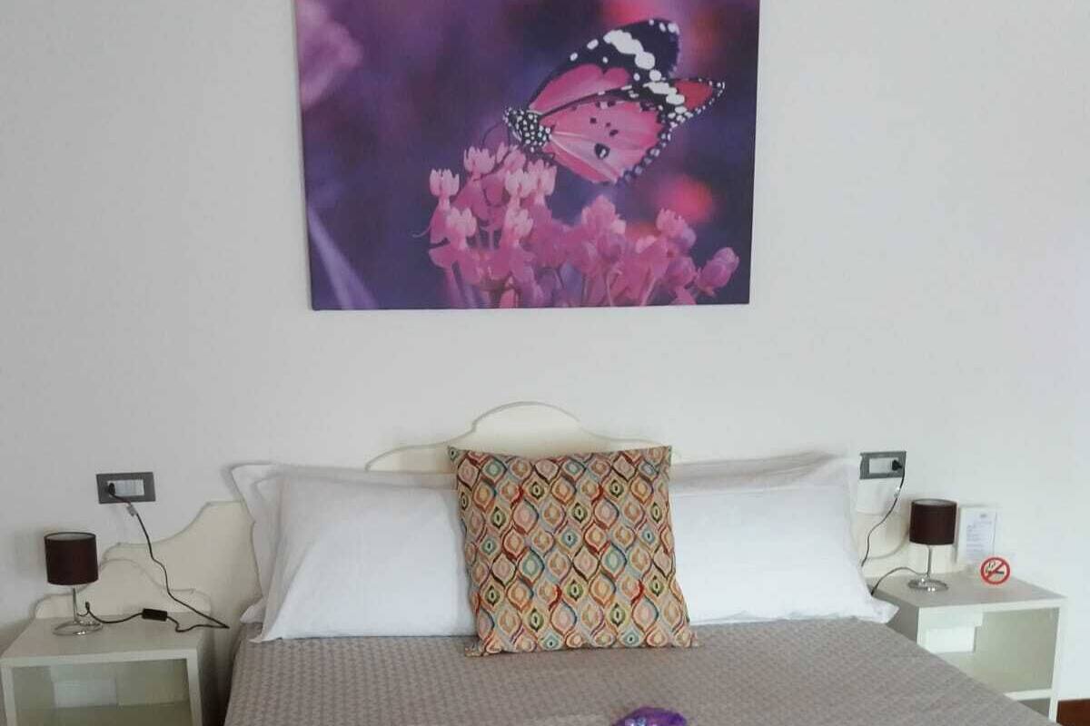 A bedroom with a bed, two bedside tables, a pillow, a wall-mounted artwork, and a nightstand with a lamp.