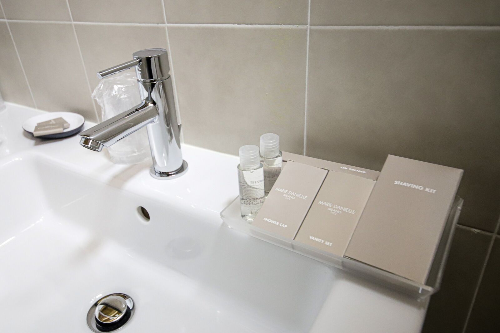A bathroom sink with a chrome faucet, a soap dish, and a vanity organizer holding Marie Daniele brand toiletries.