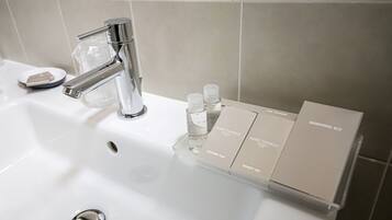 A bathroom sink with a chrome faucet, a soap dish, and a vanity organizer holding Marie Daniele brand toiletries.