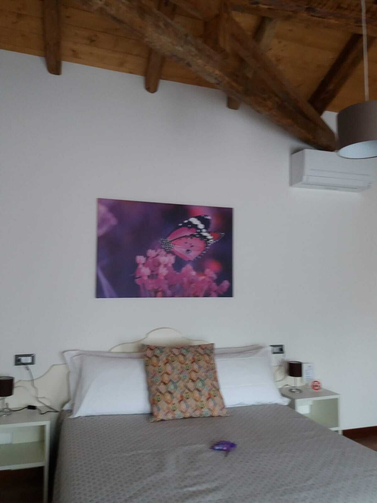 A bedroom with a bed, white nightstands, a patterned pillow, and a wall-mounted painting.