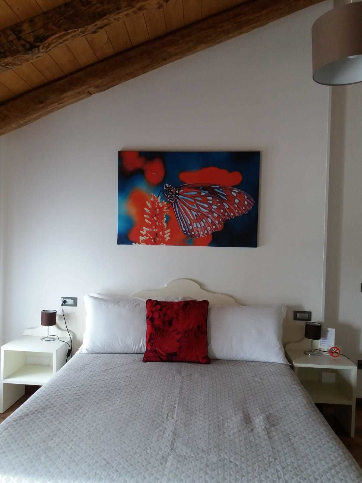 Un dormitorio con una cama, dos mesitas de noche, un cojín rojo y un cuadro colgado en la pared de una mariposa.