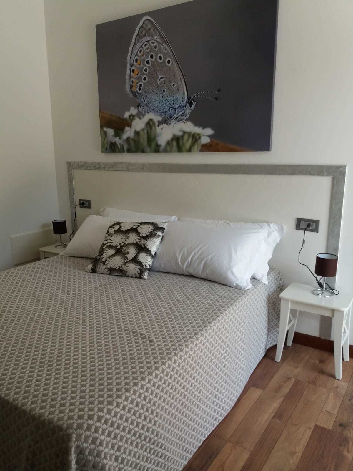 A bedroom with a large bed, a nightstand, a wall-mounted painting, and a small table with a lamp.