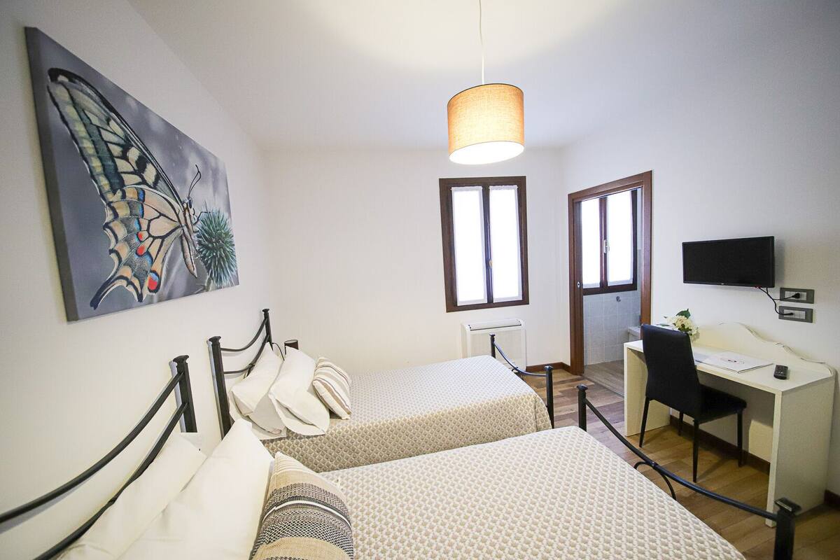 A room with two beds, a desk, a chair, a television, and a window.