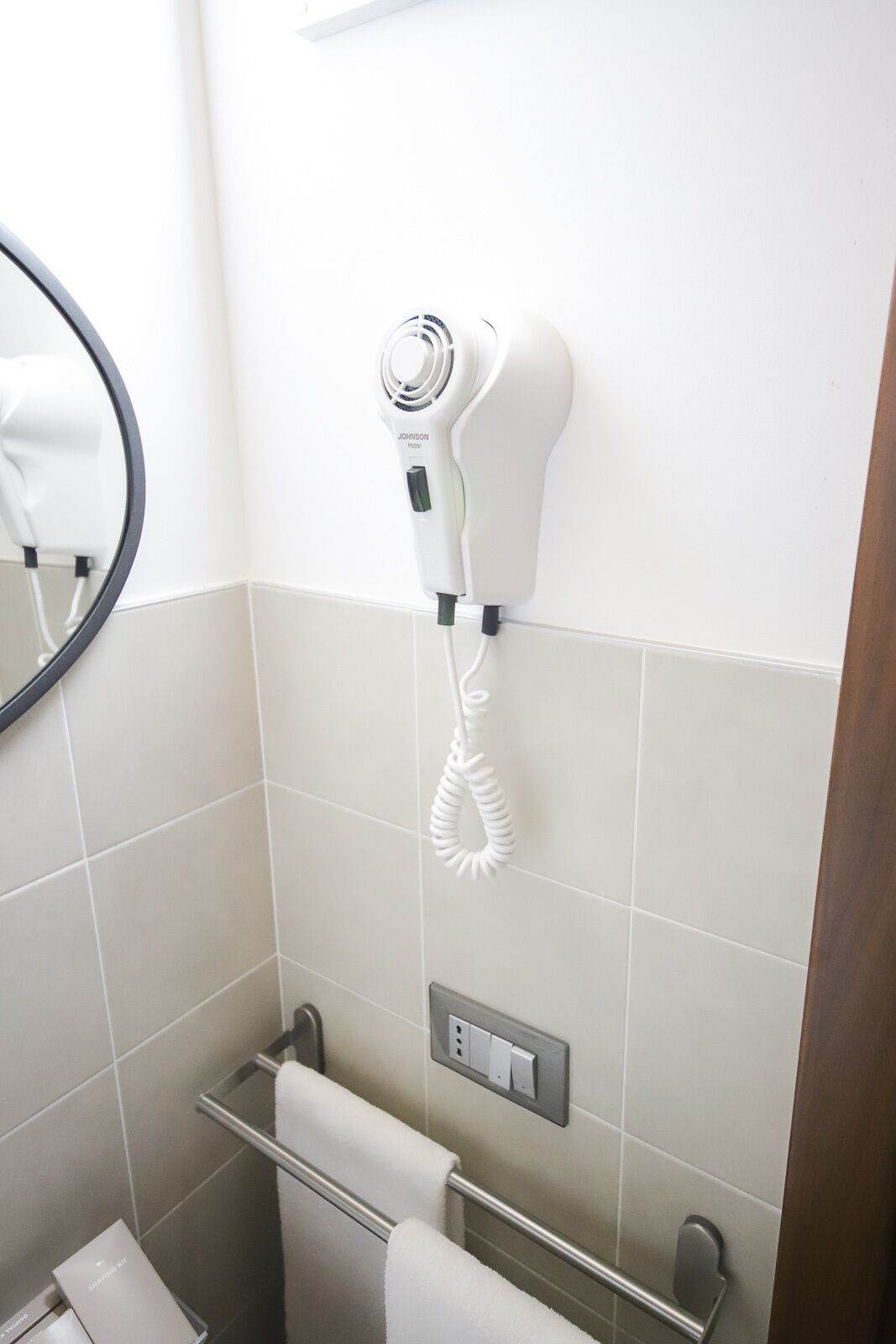 A bathroom with a hairdryer mounted on the wall, a towel rack, and a towel dispenser.