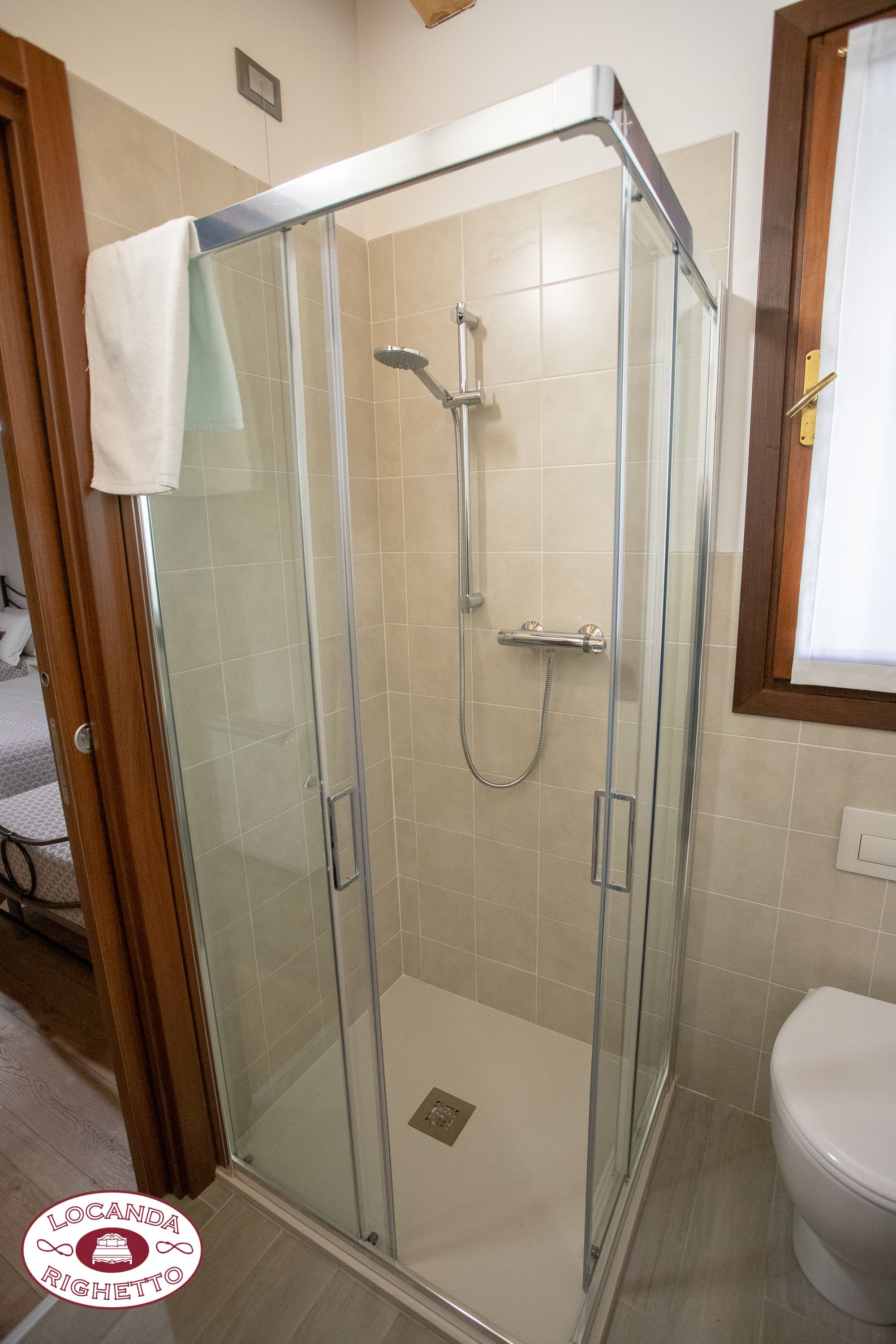 A glass-enclosed shower stall with a handheld showerhead and a handheld faucet.