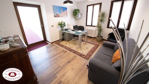 A living room with a sofa, a desk with a computer, and a dining area with a table and chairs. - Locanda Righetto (Quinto di Treviso)