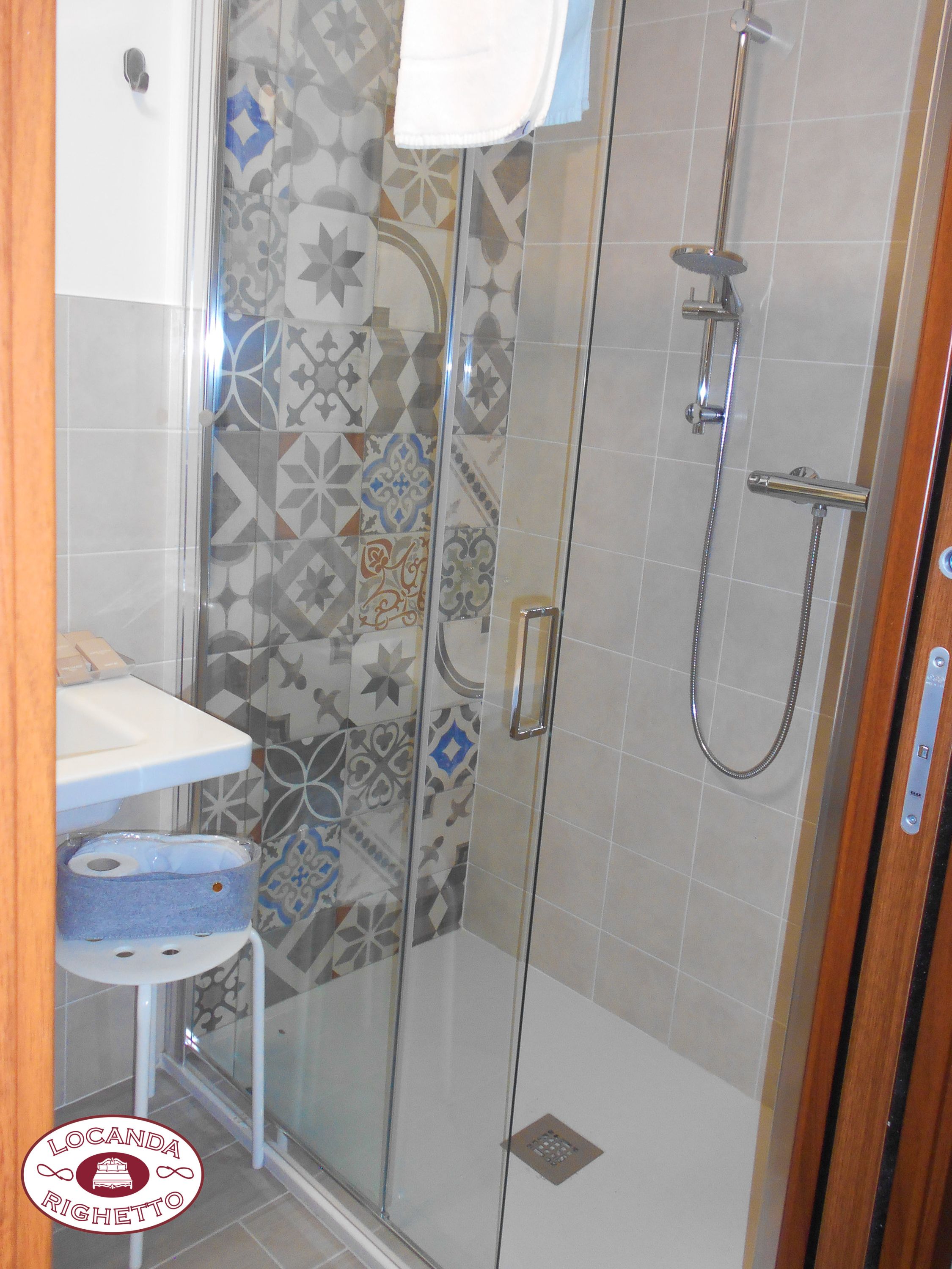 Een douche met glazen deur, een wit wastafelmeubel en een betegelde muur met patroon.