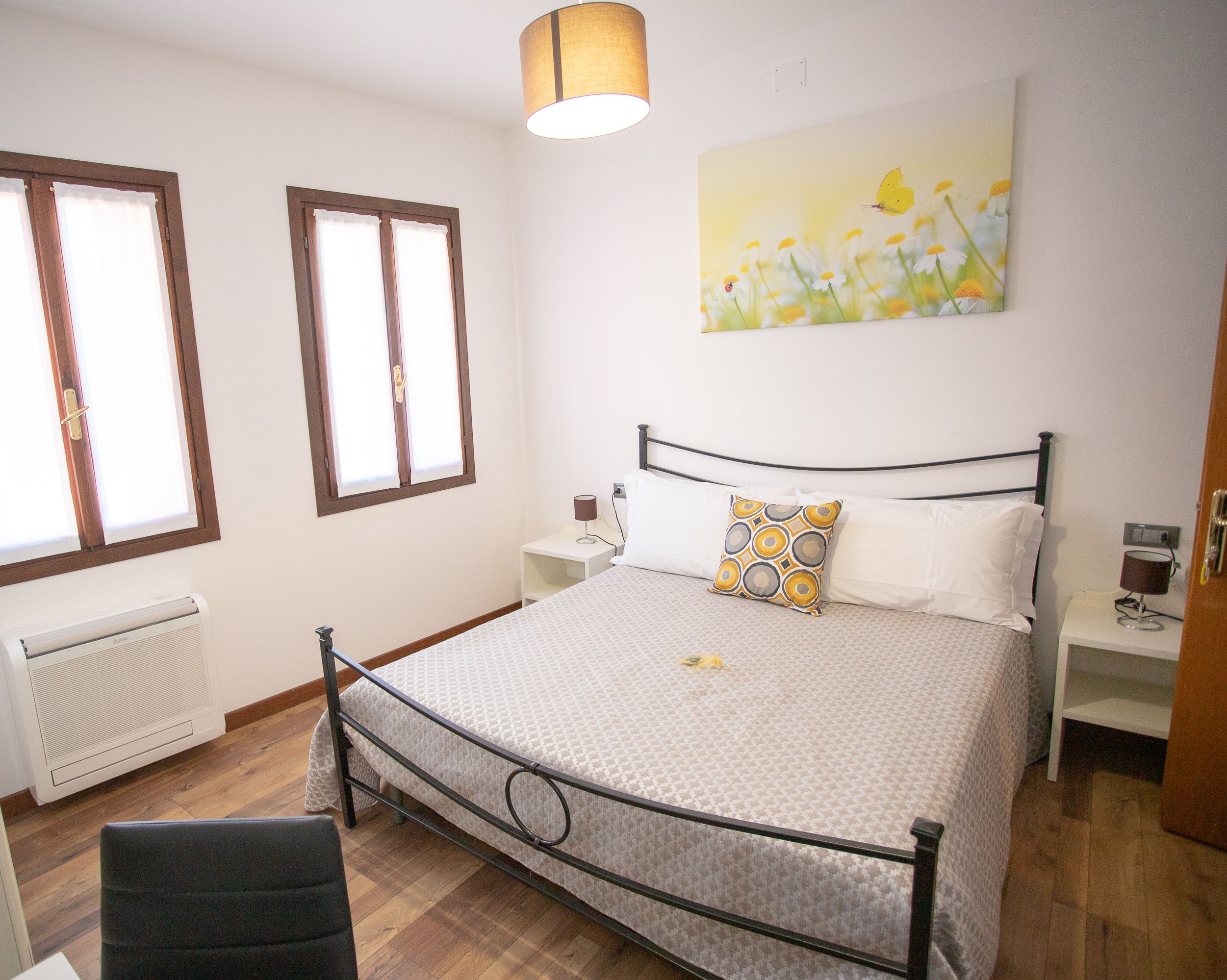Een slaapkamer met een bed, twee nachtkastjes, een stoel, een radiator en een raam.