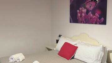 Cama bem arrumada com toalhas enroladas, um travesseiro vermelho e um quadro de uma borboleta na parede.