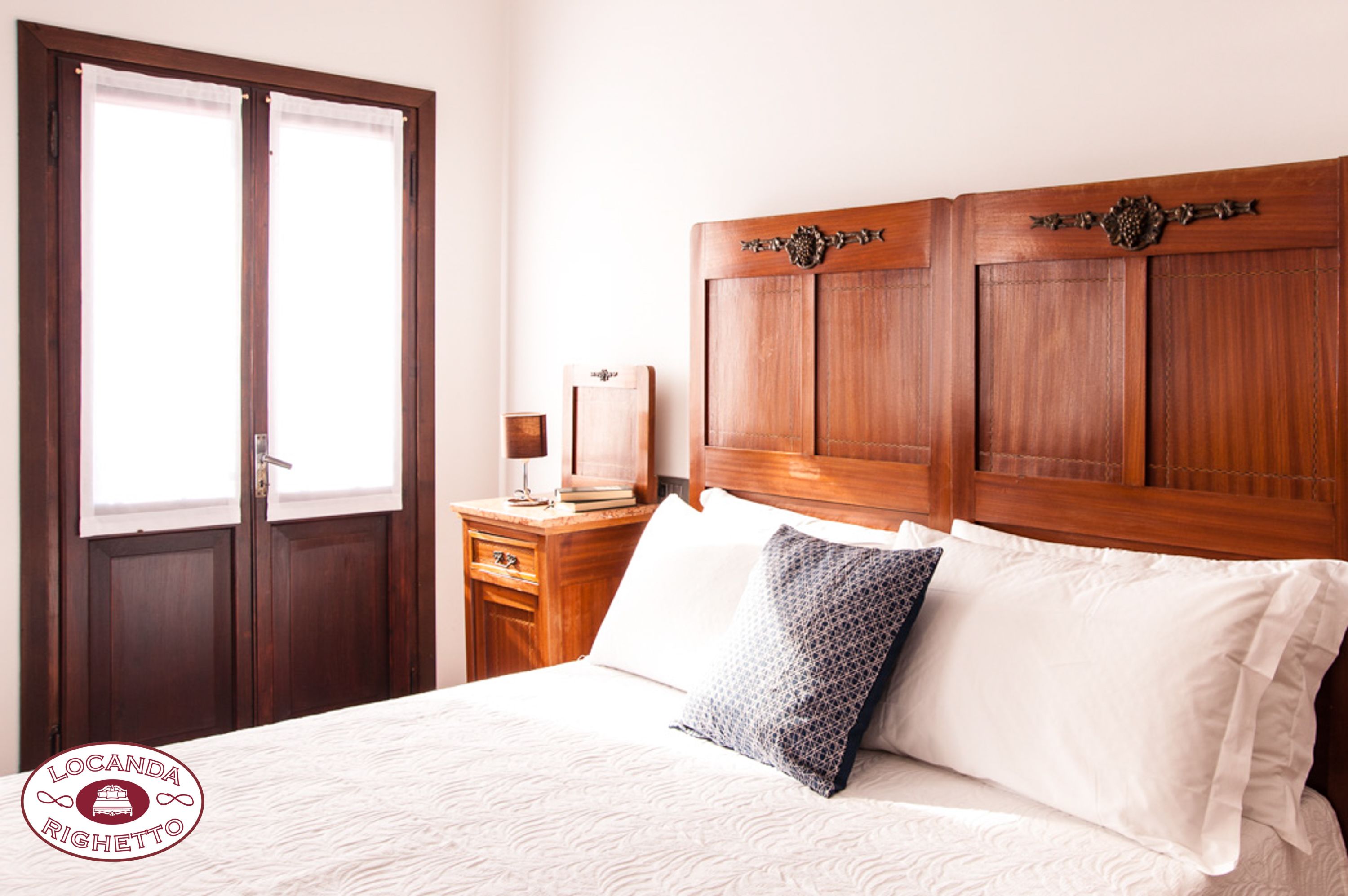Quarto com cabeceira de madeira, mesa de cabeceira com abajur e duas almofadas.