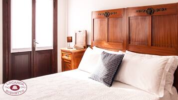 Quarto com cabeceira de madeira, mesa de cabeceira com abajur e duas almofadas.