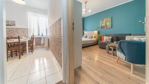 A modern living room with a blue accent wall, a sofa, a coffee table, and a dining area with a brick wall and wooden chairs. - Apartament Przytulny –2 sypialnie w centrum Starówki Gdańskiej (Gdansk)