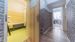A modern bathroom with a bathtub, a wooden door, and a brick wall. - Apartament Przytulny –2 sypialnie w centrum Starówki Gdańskiej (Gdansk)