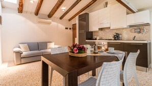A modern kitchen with white cabinets, a dining table with white chairs, and a wooden ceiling. - Corderie de la Tana Biennale Exhibition (Venice)