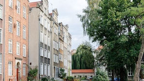 A row of multi-story buildings with a mix of architectural styles, including brick and stucco facades, and a tree-lined street. - Apartament Przytulny – centrum Starówki Gdańskiej (Gdansk)