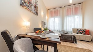 A modern living room with a dining area, featuring a sofa, a coffee table, and a painting on the wall. - Apartament Przytulny – centrum Starówki Gdańskiej (Gdansk)