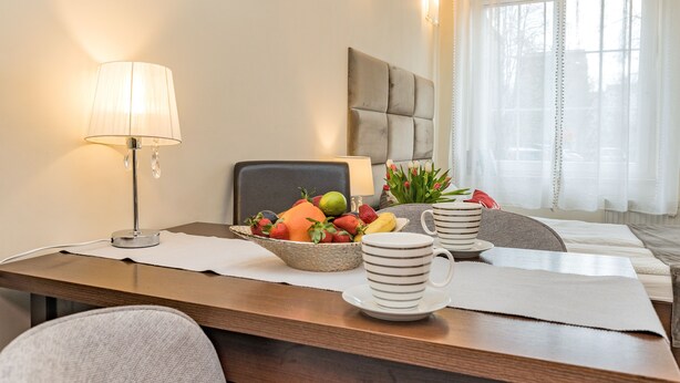 A hotel room with a dining table set with a fruit bowl, a lamp, and a coffee set. - Apartament Przytulny – centrum Starówki Gdańskiej (Gdansk)