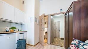 A compact room with a kitchenette, a suitcase, a bed with a floral pillow, and a wardrobe. - Apartament Przytulny – centrum Starówki Gdańskiej (Gdansk)