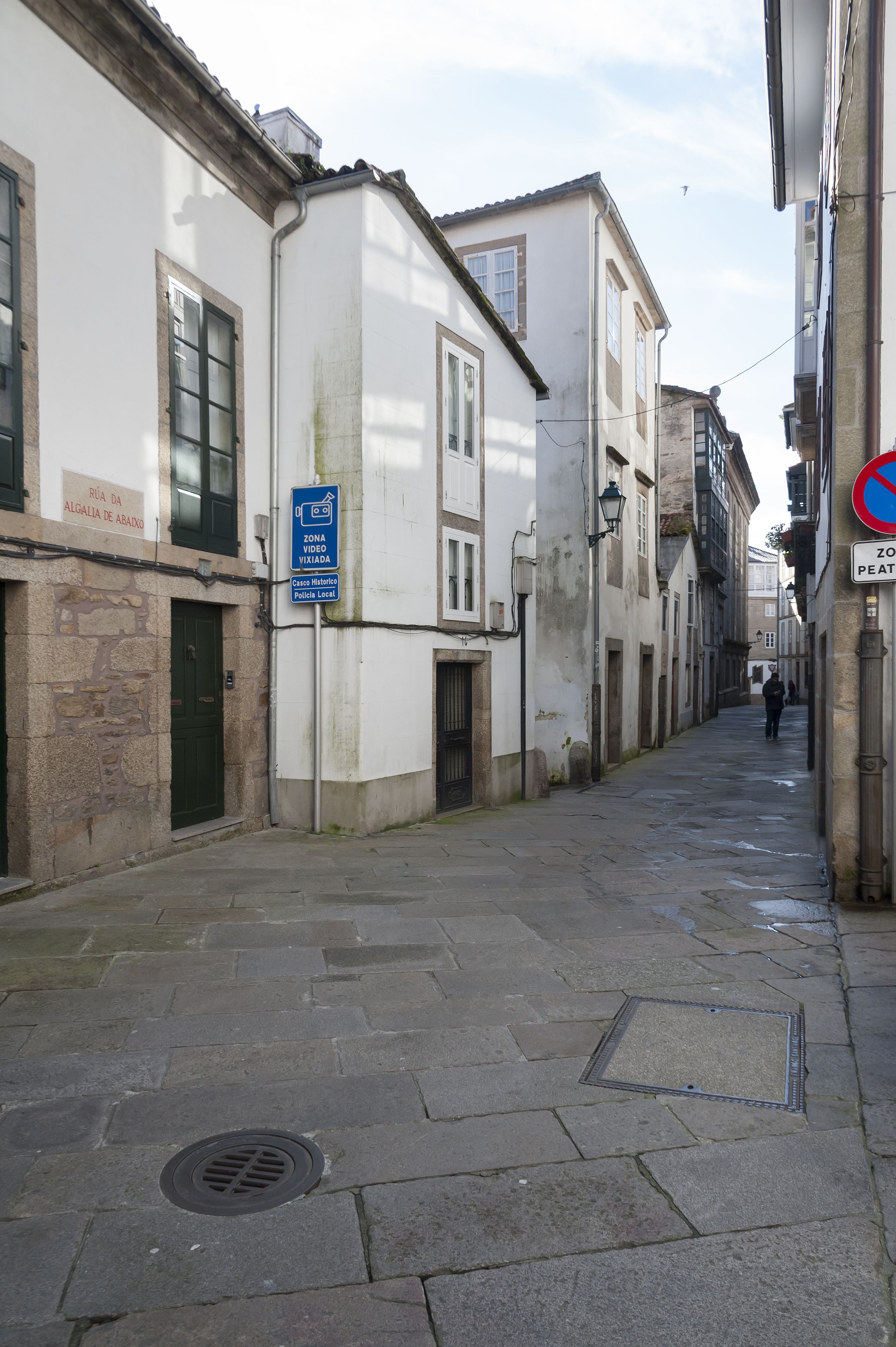 Una calle estrecha con edificios históricos, una tapa de alcantarilla y un letrero azul que indica una zona de video.