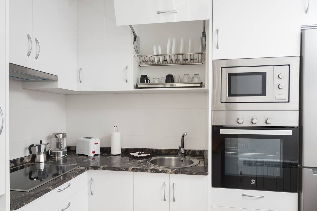 A modern kitchen with white cabinets, a stainless steel oven, a microwave, and a sink.