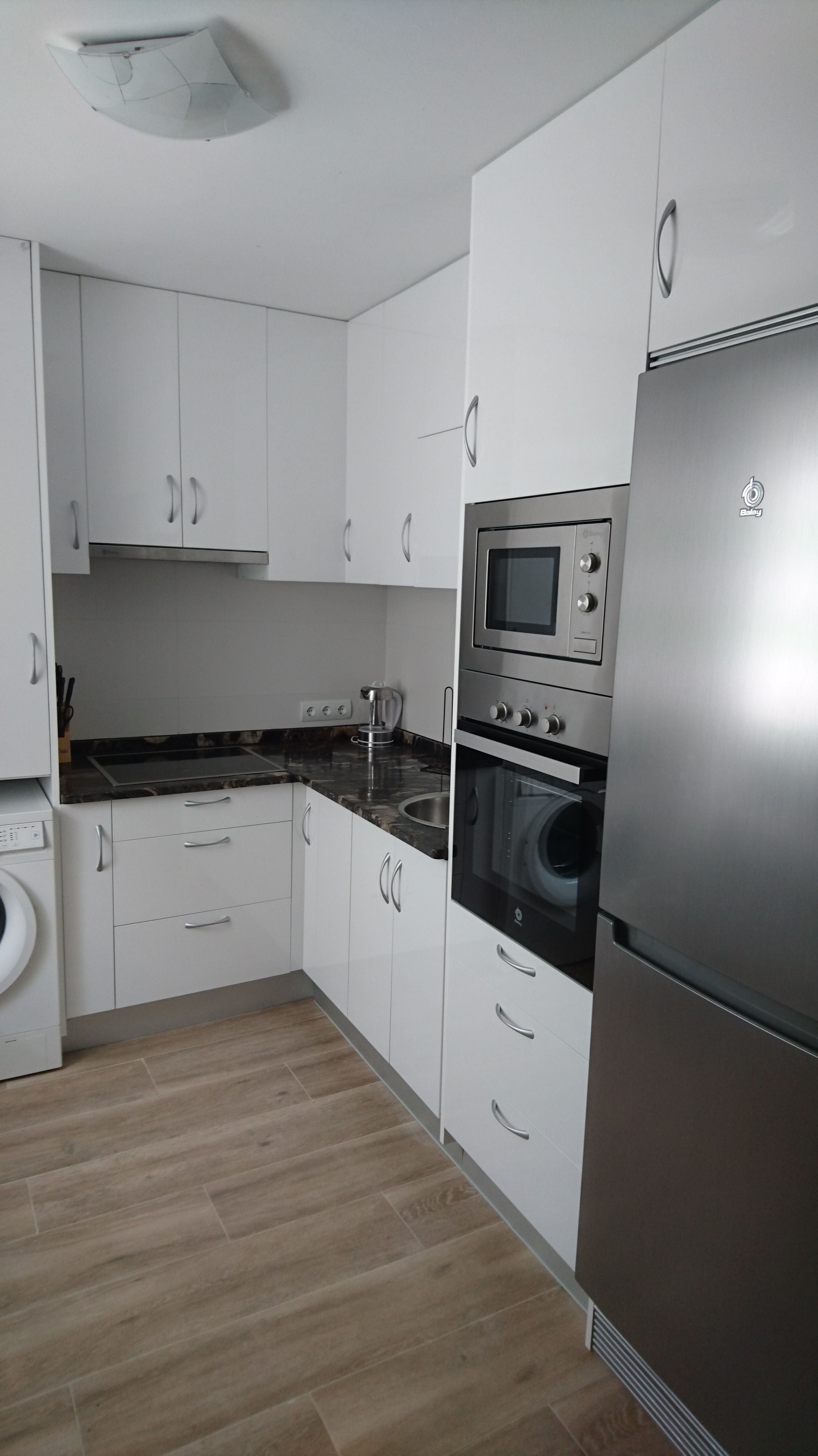 A modern kitchen with white cabinets, a stainless steel refrigerator, a built-in oven, and a microwave.