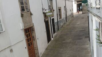 A narrow street with stone pavement, white buildings with multiple windows, and a visible door on the left.
