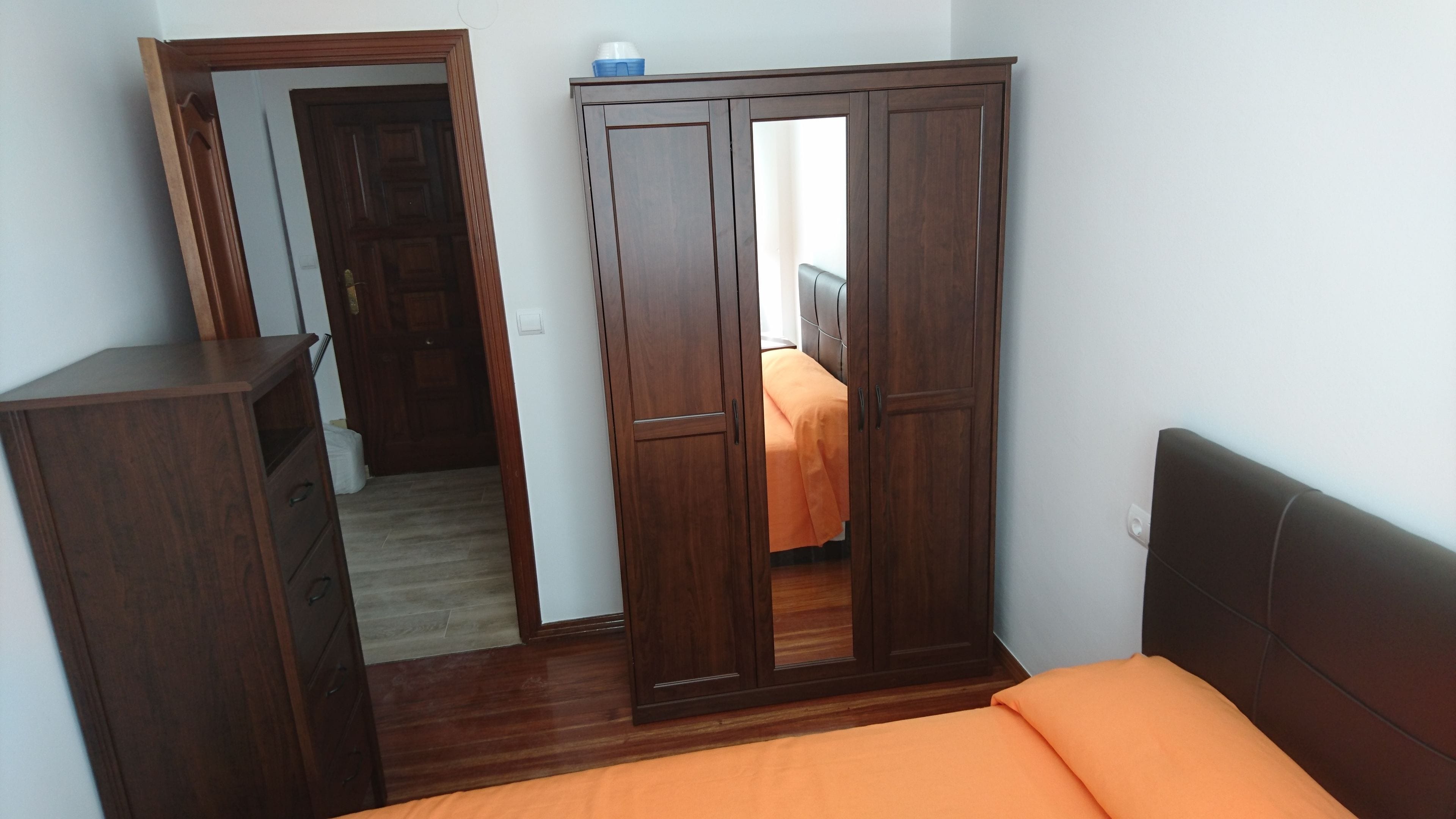 Un dormitorio con un armario de madera, una cama con colcha naranja y un espejo.