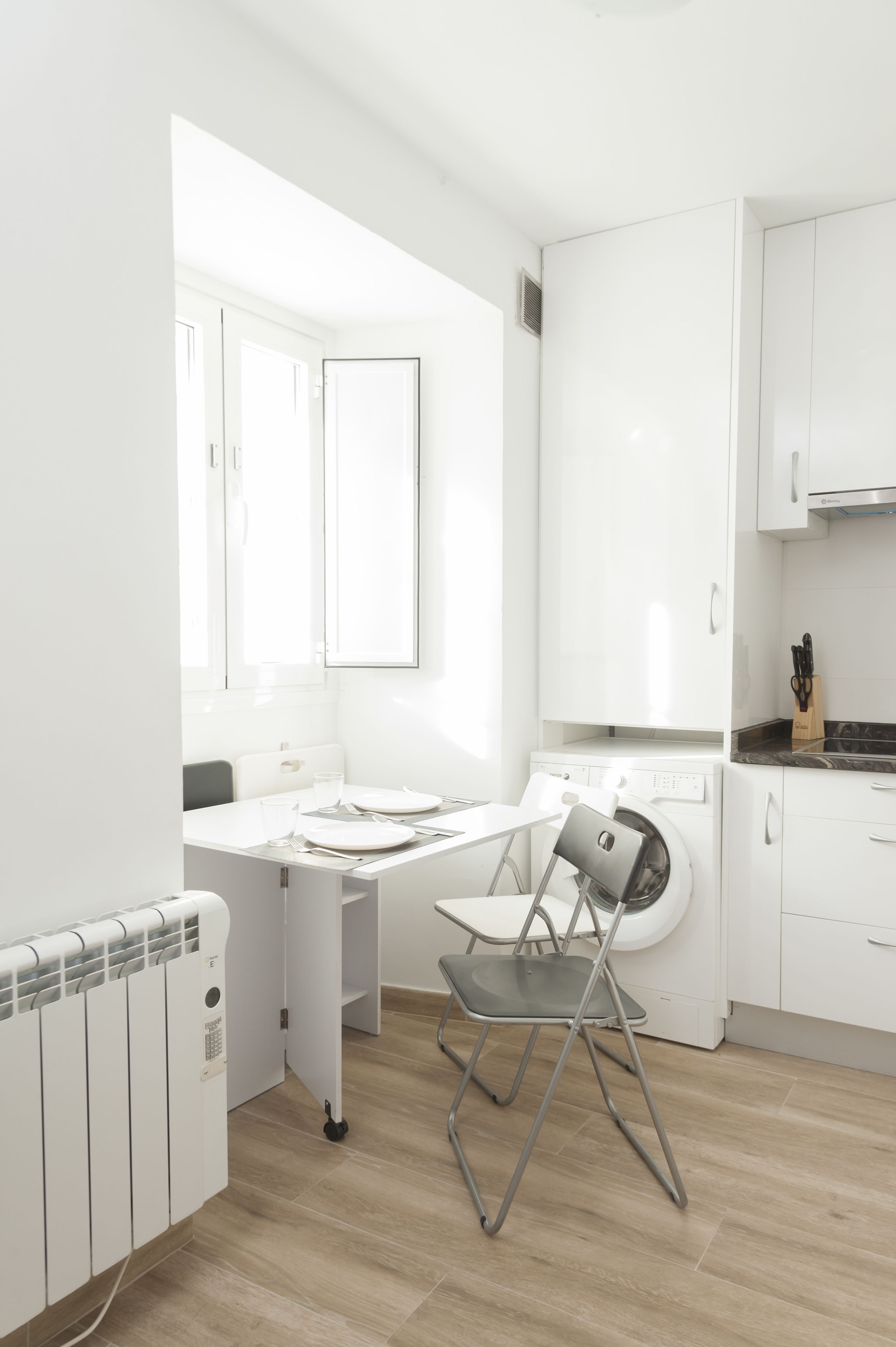A modern kitchen with a built-in washing machine, a dining table with chairs, and a radiator.