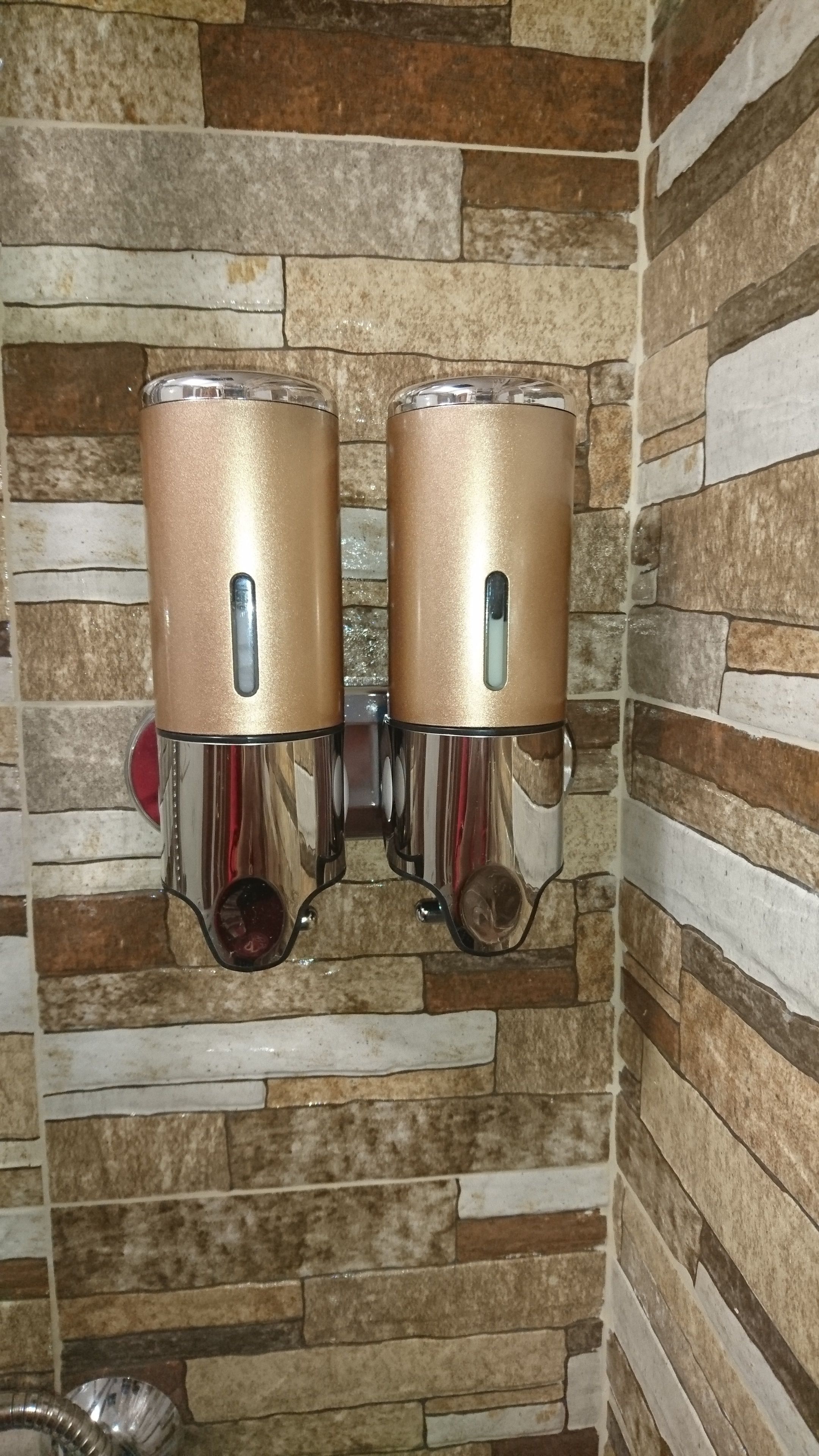 A bathroom with a stone wall and two gold-colored towel dispensers mounted on it.