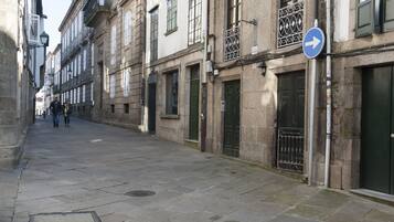 A narrow street lined with historic buildings, featuring stone facades, balconies, and a directional sign.