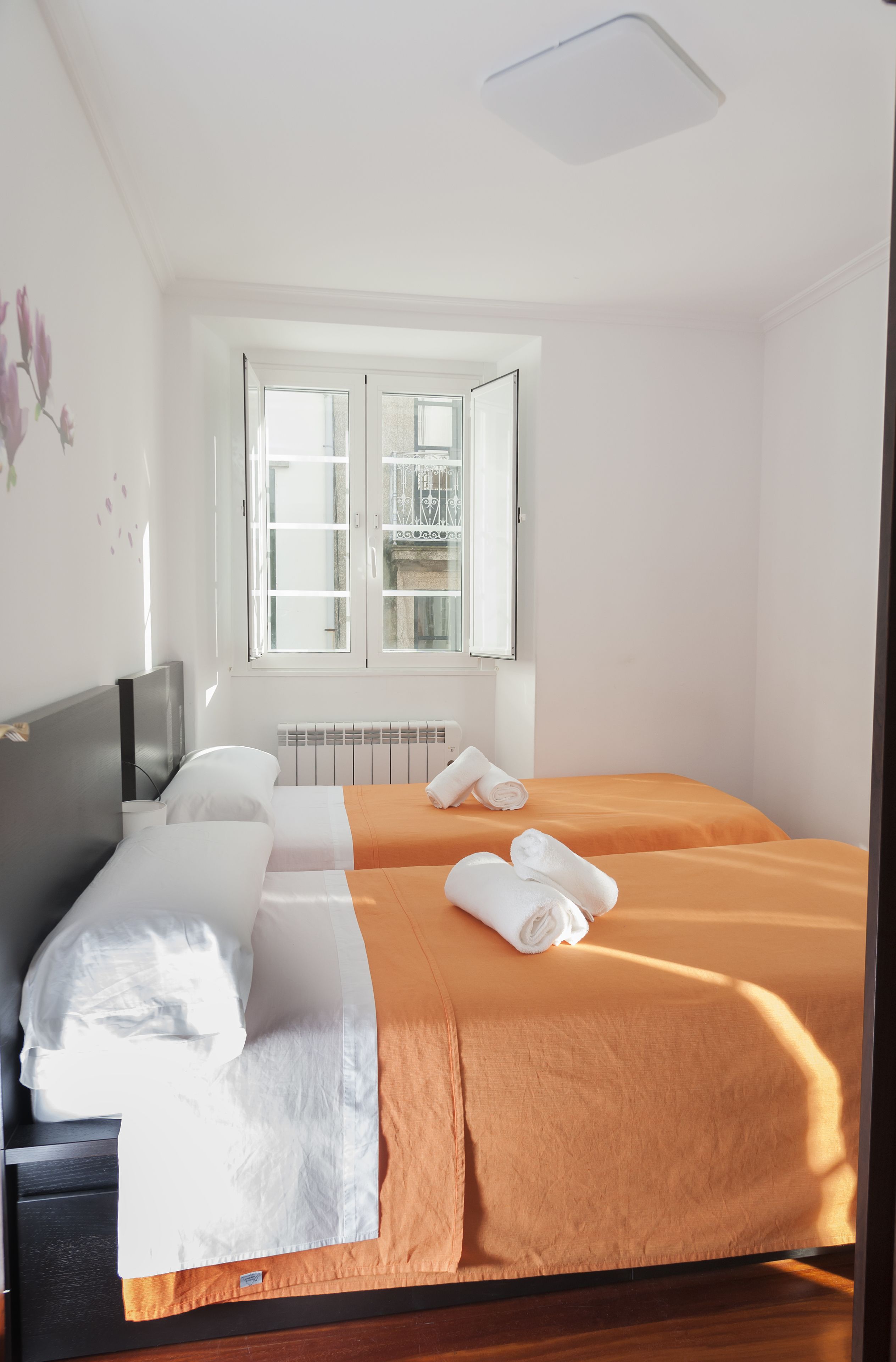 A hotel room with two beds, a window, a radiator, and a television on a stand.