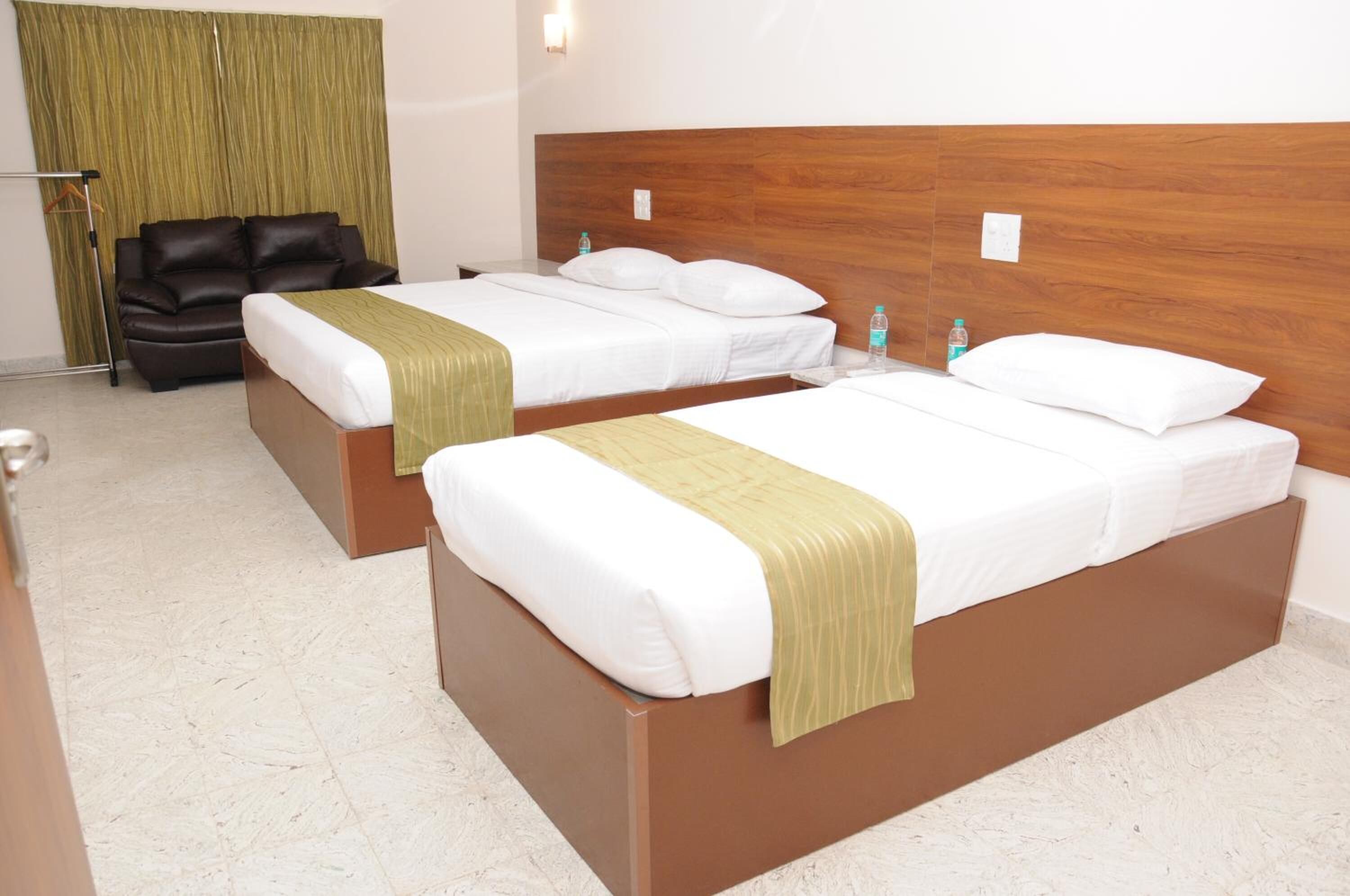 Two single beds with wooden headboards, a brown sofa, and a green curtain in a hotel room.