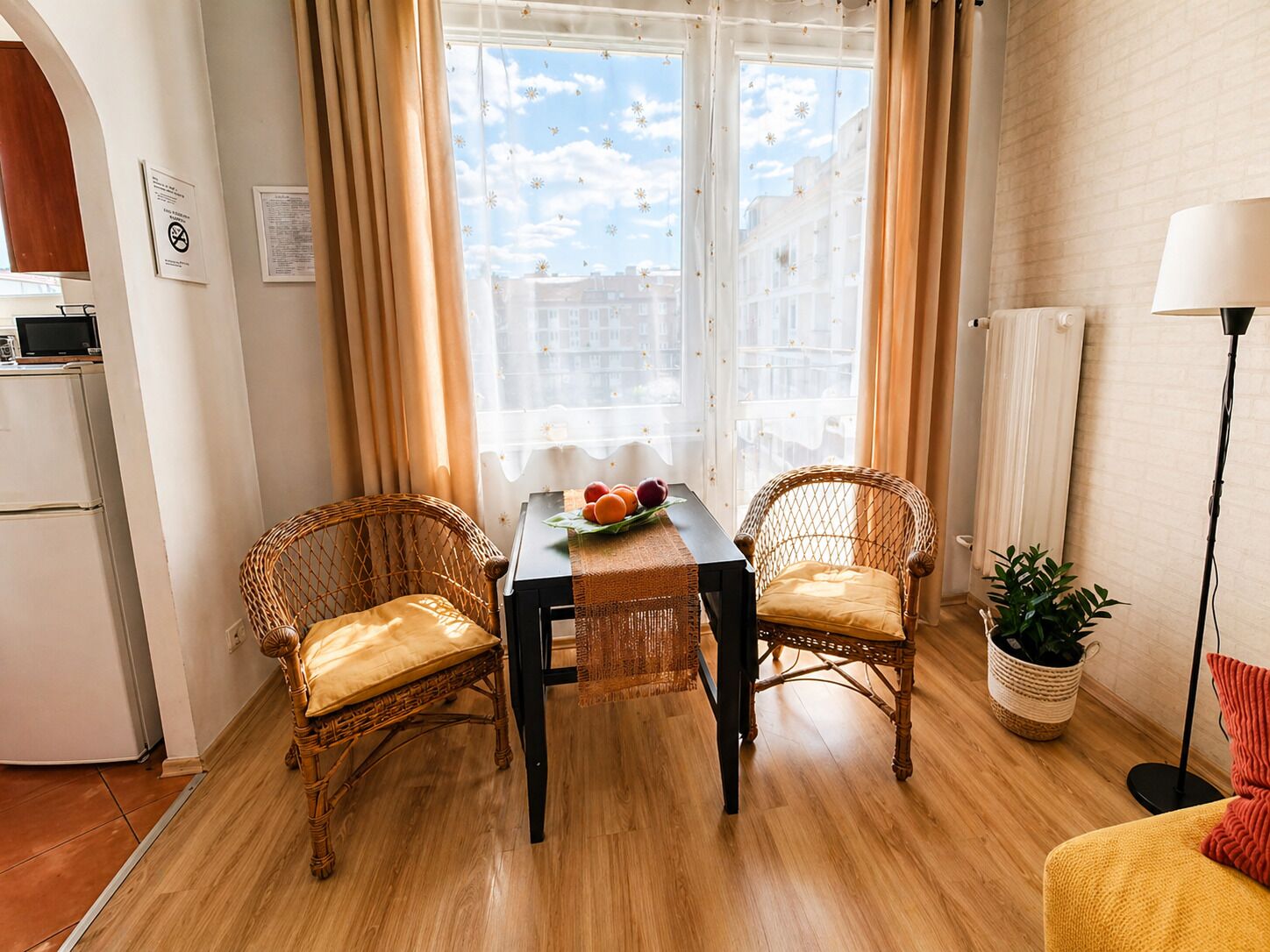 A cozy room with a dining table, two wicker chairs, a potted plant, and a lamp.