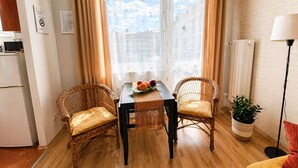 Een gezellige kamer met een eettafel, twee rieten stoelen, een potplant en een lamp.