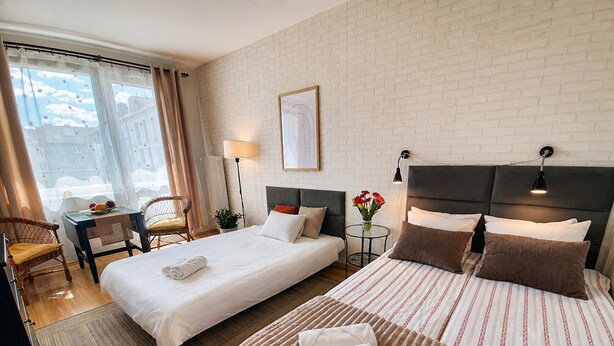 Een hotelkamer met twee bedden, een bureau, een stoel, een lamp en uitzicht op gebouwen.