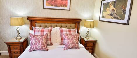 A neatly made bed with a wooden headboard, two bedside tables with lamps, and two framed pictures on the wall.