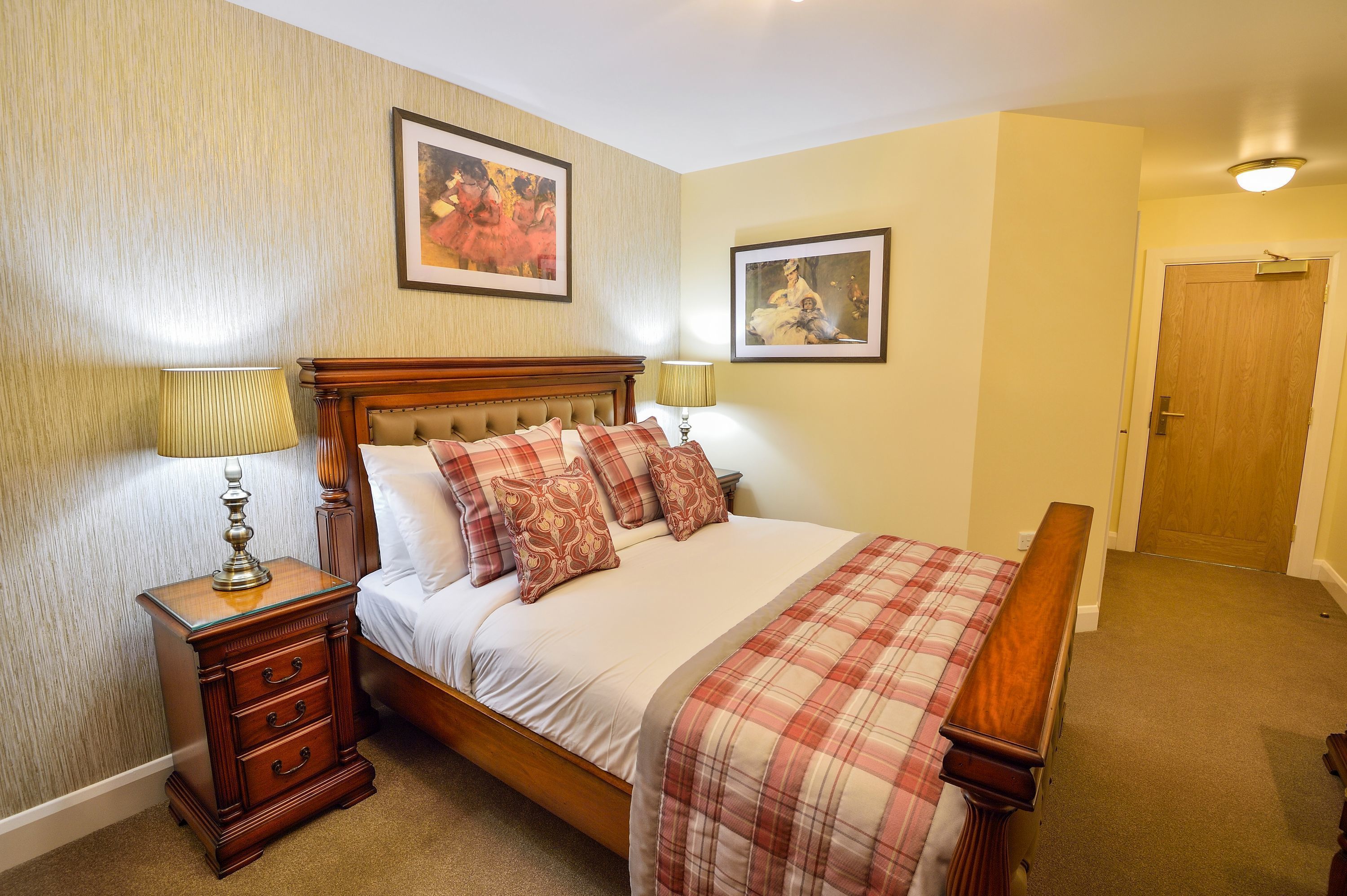A bedroom with a wooden bed, two bedside tables with lamps, a wooden bench, and two framed pictures on the wall.