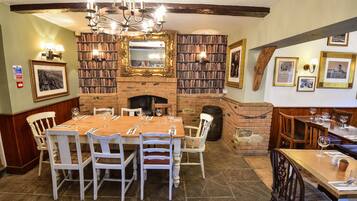 A dining area with a brick fireplace, wooden tables, and chairs.