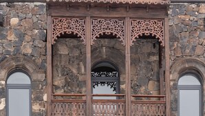 Un edificio con fachada de piedra, balcón de madera con celosías elaboradas y tres ventanas con persianas de madera.