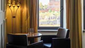 Una habitación con una mesa redonda, dos sillas, una lámpara y un amplio ventanal arqueado con cortinas.