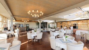 Un restaurante espacioso con techos de madera, mesas y sillas blancas y una zona de bar.