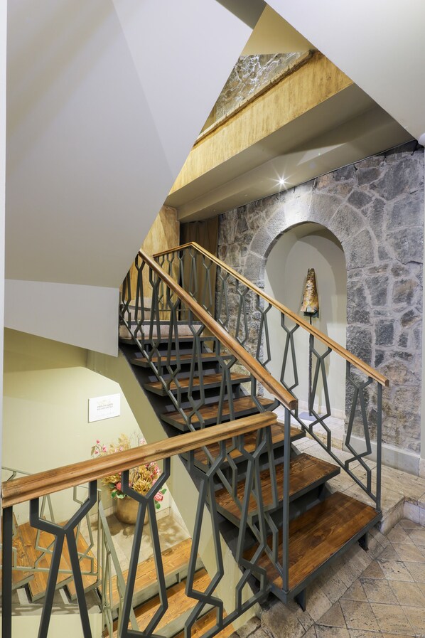 A staircase with a geometric metal railing and wooden steps, leading to a stone wall with an arched niche.