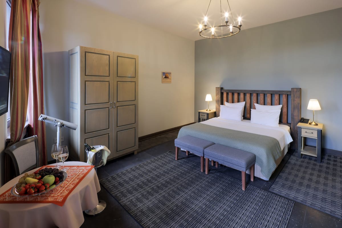 A hotel room with a bed, bedside tables, a desk with a chair, a television, and a fruit basket.